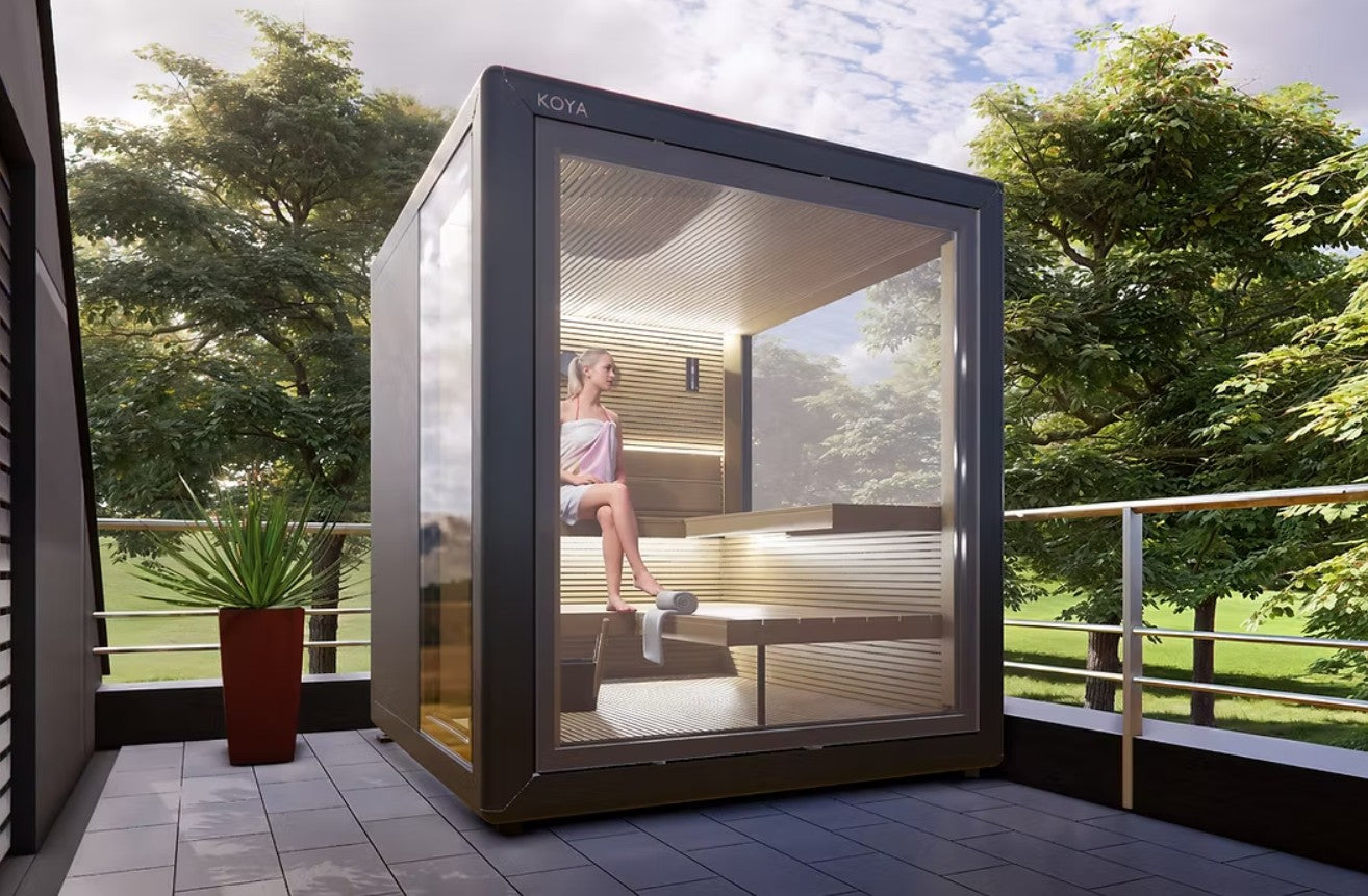 Portable Koya Modern Cube Outdoor Traditional Sauna on a balcony with a person inside, surrounded by greenery.