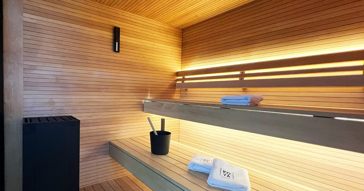 Koya Modern Cube Outdoor Traditional Sauna - interior view with a shelf, towels, and a black container.